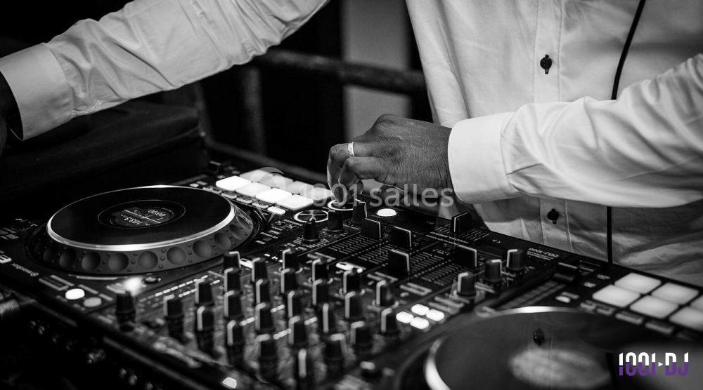 Un DJ ajuste les réglages sur une table de mixage lors d'une performance en noir et blanc.