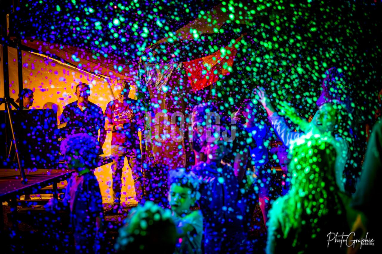 Des personnes dansent sous des lumières colorées et des projections de mousse lors d'un événement festif nocturne.