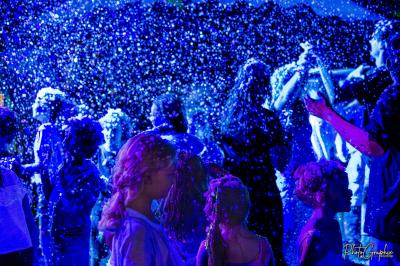 Groupe de personnes réunies en soirée en plein air, éclairées par des guirlandes lumineuses et des lampadaires.