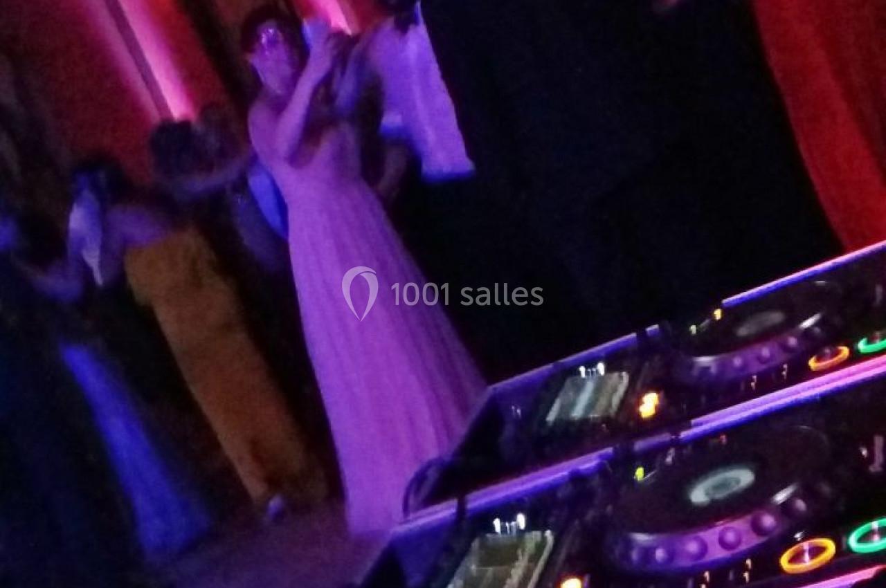 Vue d'une piste de danse animée avec des invités élégants, prise depuis une table de mixage en premier plan.