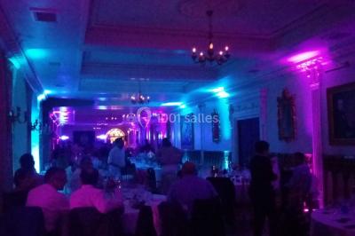 Des personnes dansent sous des lumières rouges dans une salle ornée de décorations murales et de lustres.