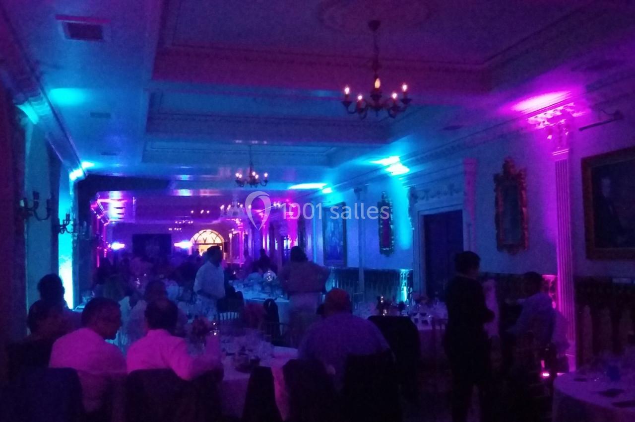 Salle de réception éclairée par des lumières colorées violettes et bleues, avec des invités assis et debout.