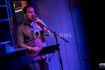 Un homme chante au micro sur une scène éclairée par des lumières bleues et violettes.
