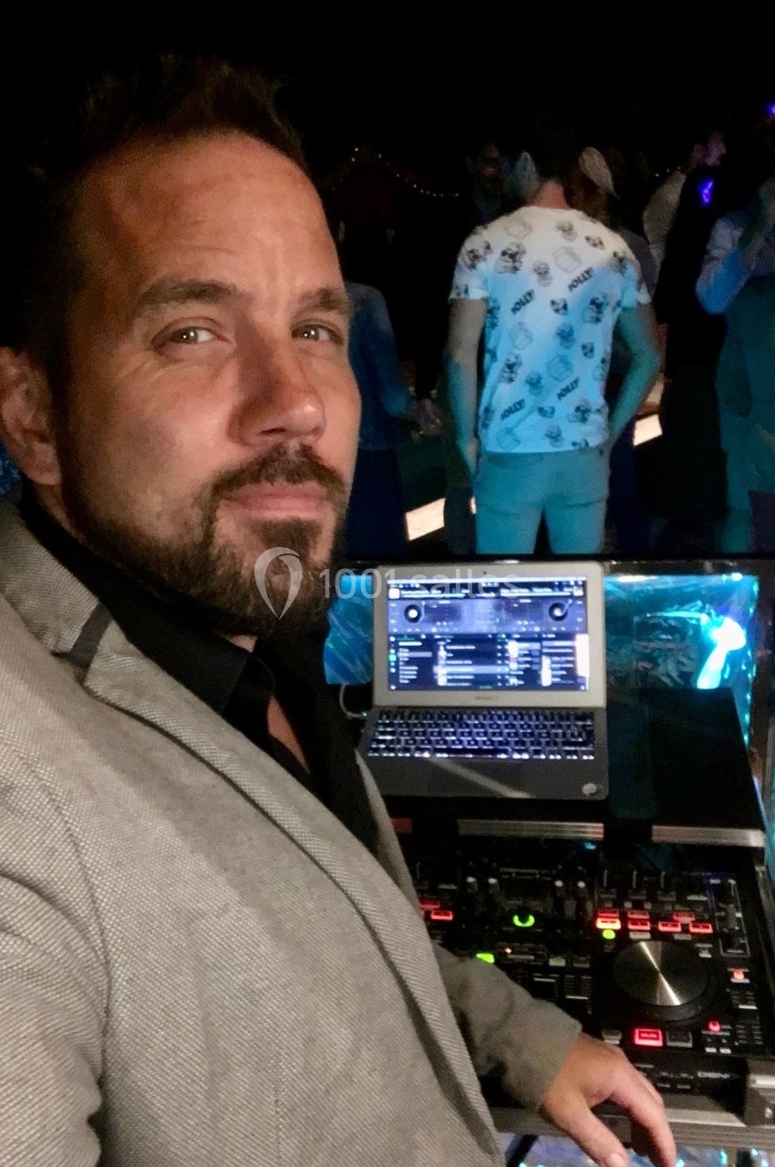 Homme en costume devant une table de mixage et un ordinateur, lors d'un événement en soirée avec des participants en arrière…