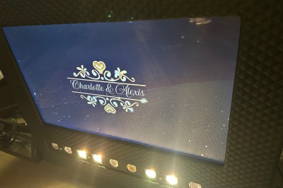 Borne de karaoké avec écran tactile affichant une interface de sélection de chansons, dans une salle animée.