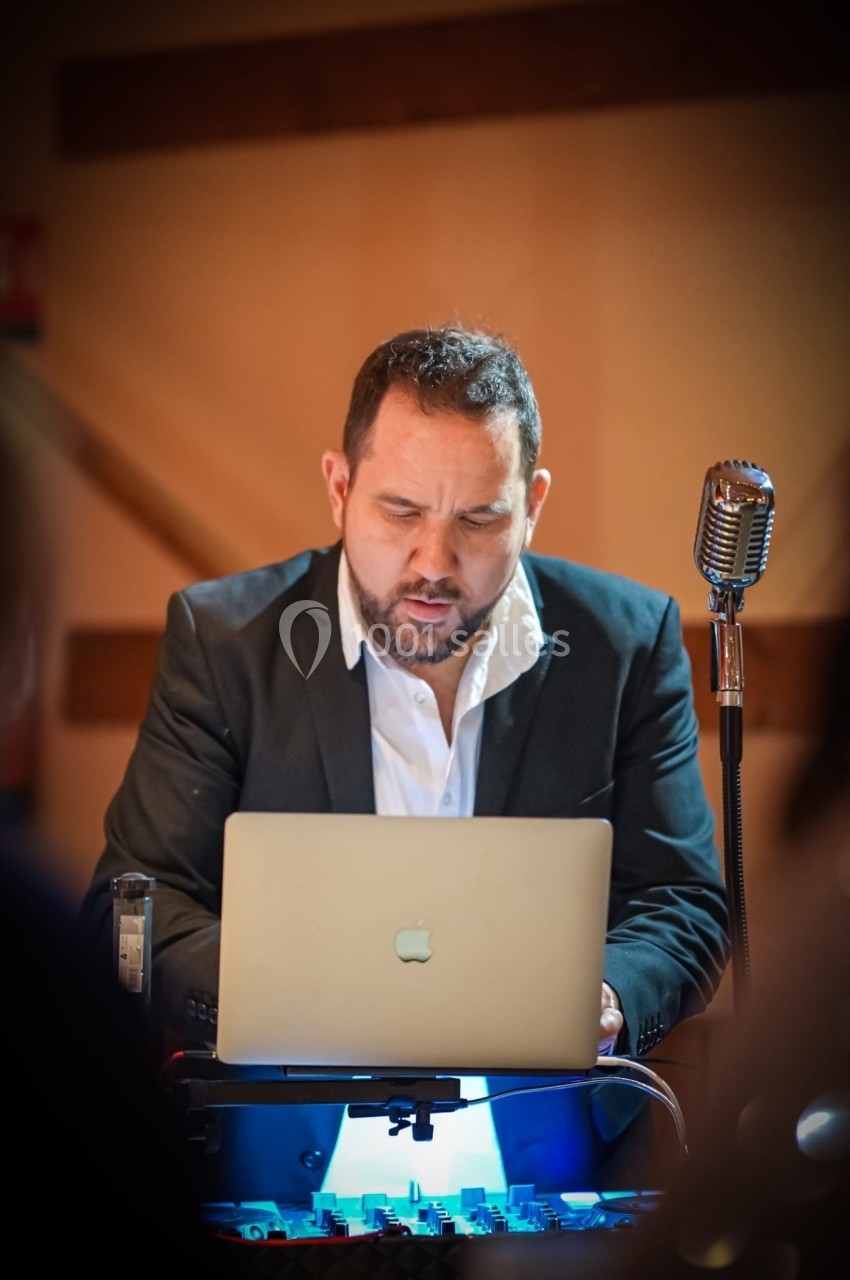 Homme en costume travaillant sur un ordinateur portable, avec un microphone rétro à proximité, dans une ambiance tamisée.