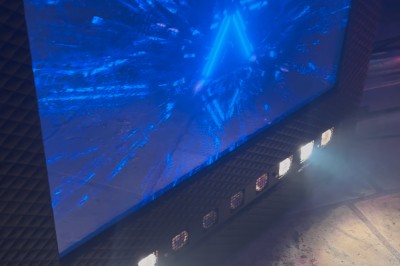 Borne de karaoké avec écran tactile affichant une interface de sélection de chansons, dans une salle animée.