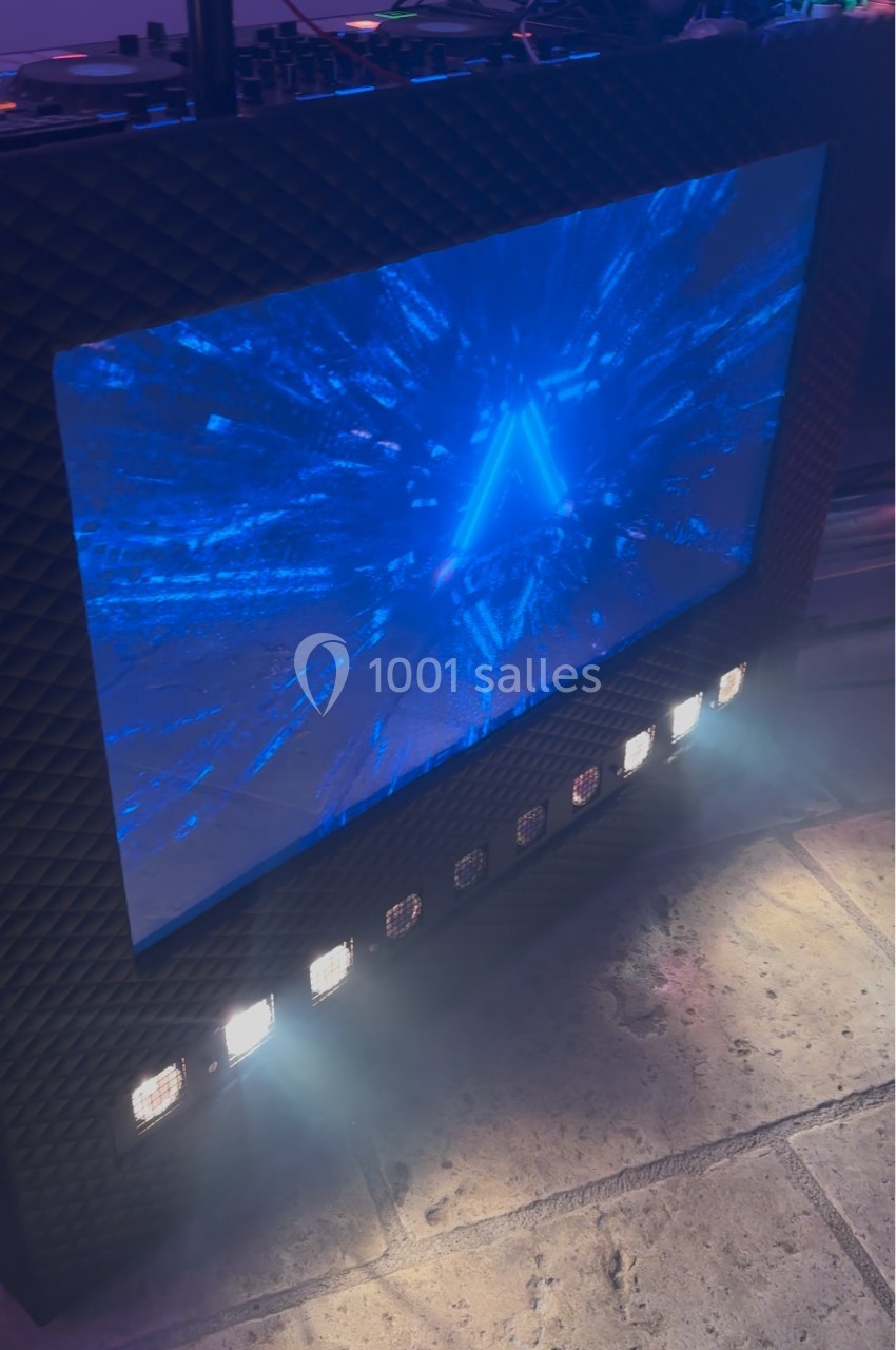 Écran lumineux affichant un graphisme bleu en forme de triangle, entouré de projecteurs LED sur un sol en pierre.