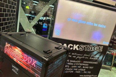 Borne de karaoké avec écran tactile affichant une interface de sélection de chansons, dans une salle animée.