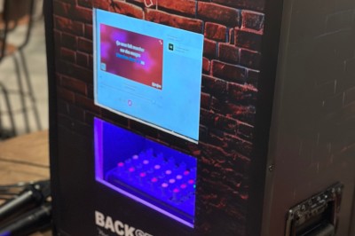 Borne de karaoké avec écran tactile affichant une interface de sélection de chansons, dans une salle animée.