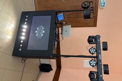 Borne de karaoké avec écran tactile affichant une interface de sélection de chansons, dans une salle animée.