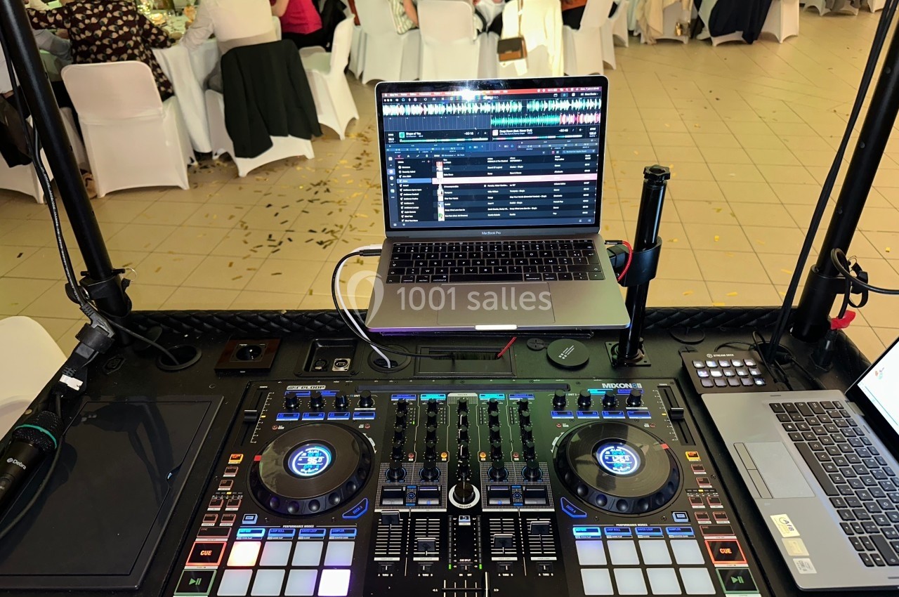 Poste de DJ avec une console de mixage, un ordinateur portable et un micro, dans une salle de réception animée.