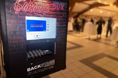 Borne de karaoké avec écran tactile affichant une interface de sélection de chansons, dans une salle animée.