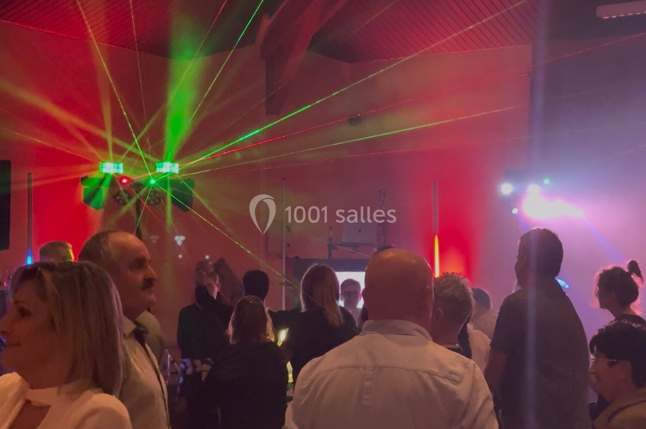 Personnes rassemblées dans une salle illuminée par des jeux de lumière colorés lors d'un événement festif.