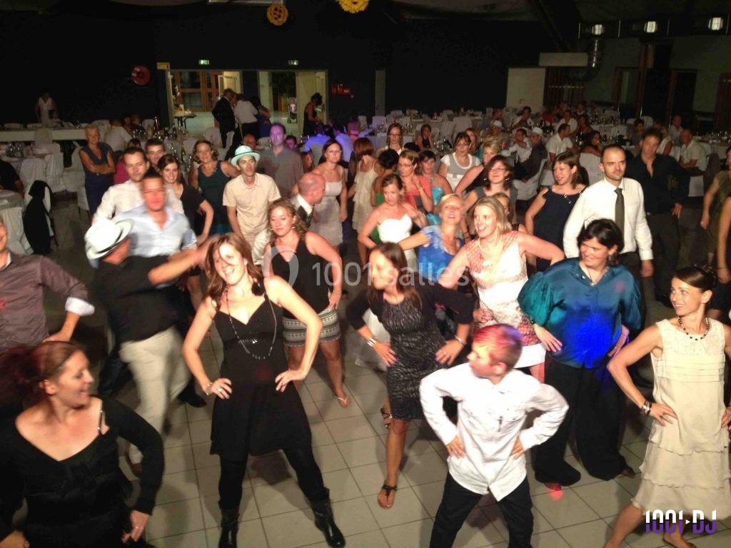 Des personnes dansent en groupe dans une salle de réception, entourées de tables et d'invités assis.