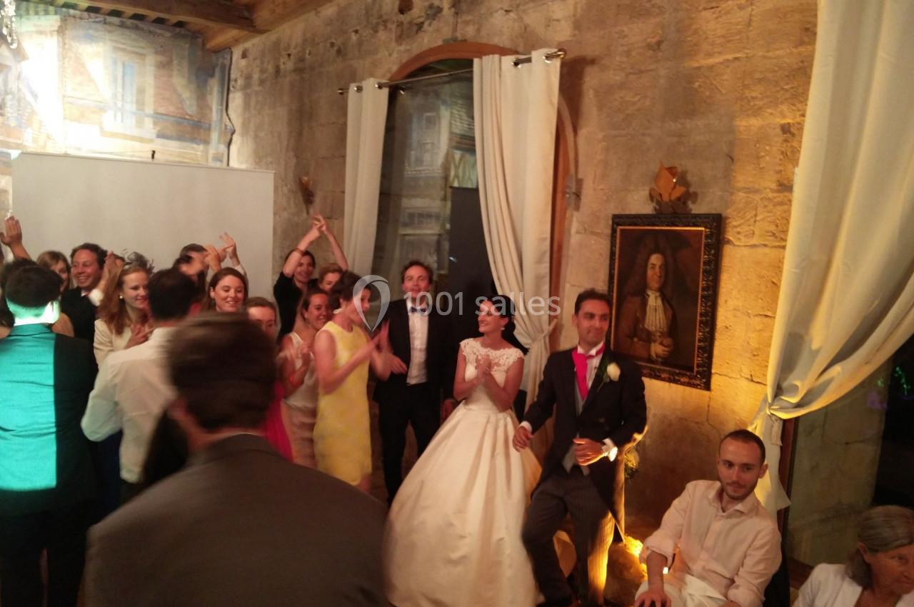 Groupe de personnes célébrant un mariage dans une salle en pierre avec des rideaux blancs et un tableau au mur.