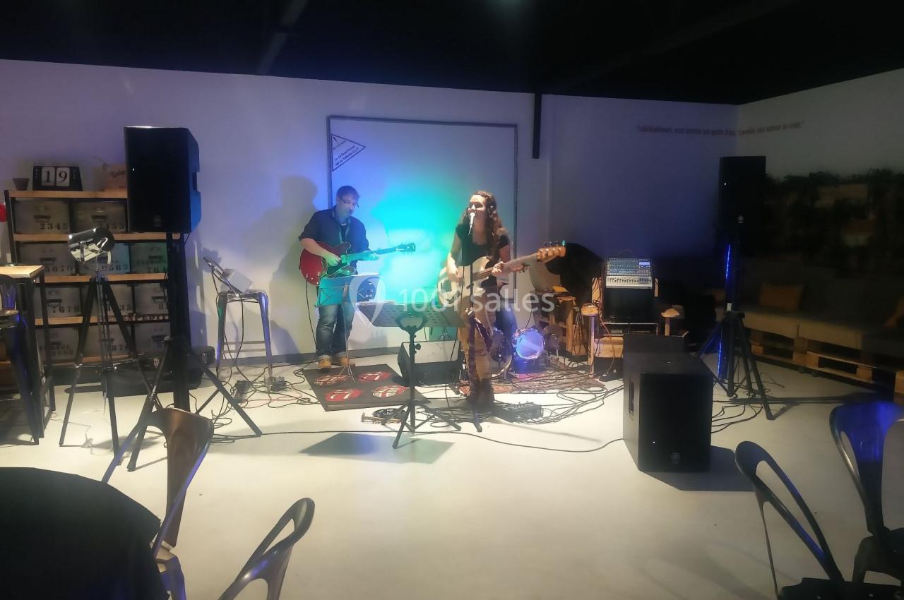 Deux musiciens jouent de la guitare sur une petite scène éclairée, entourés d'équipements audio.