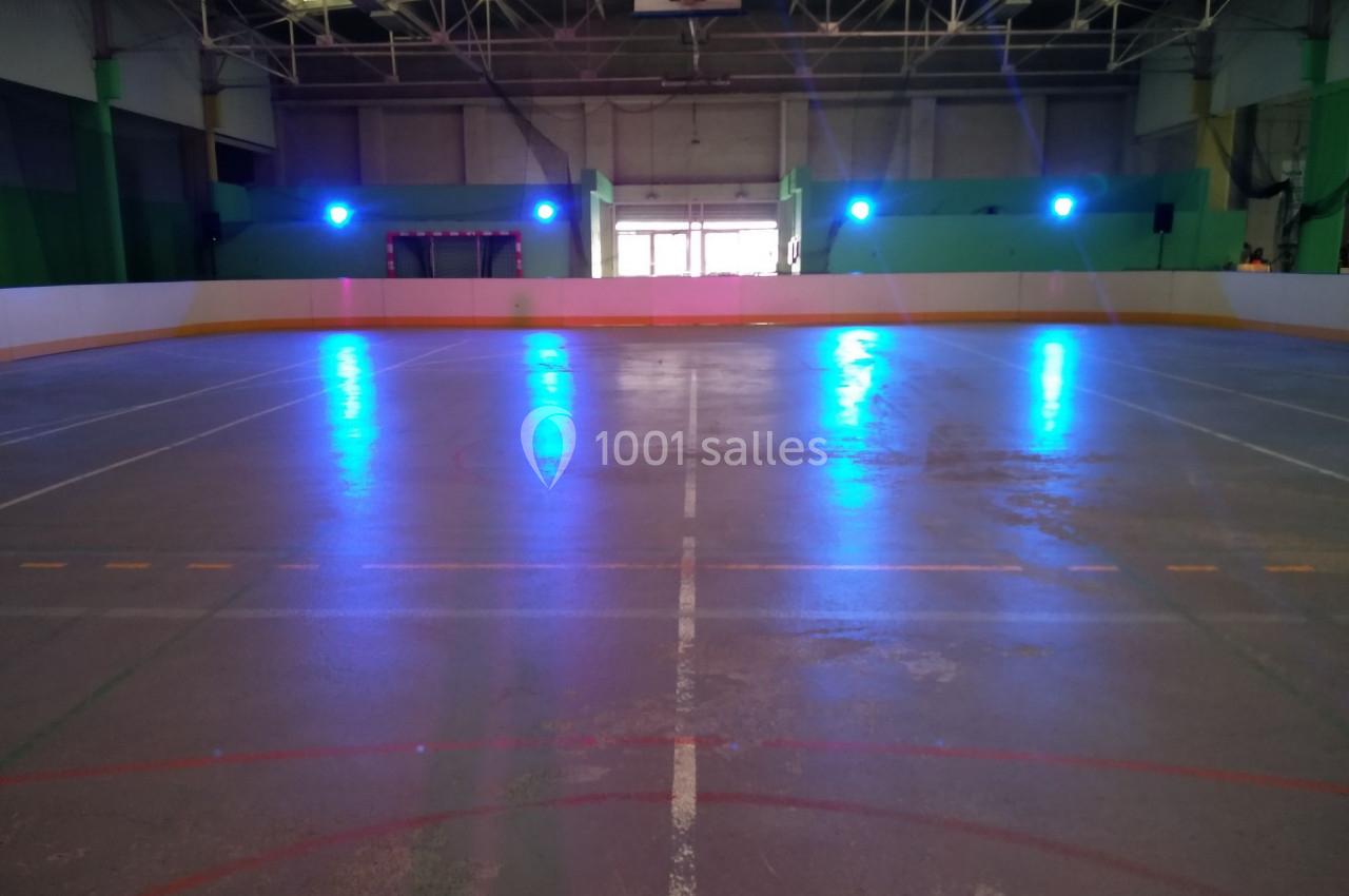Patinoire intérieure vide avec éclairage bleu, lignes marquées au sol et structure métallique visible au plafond.