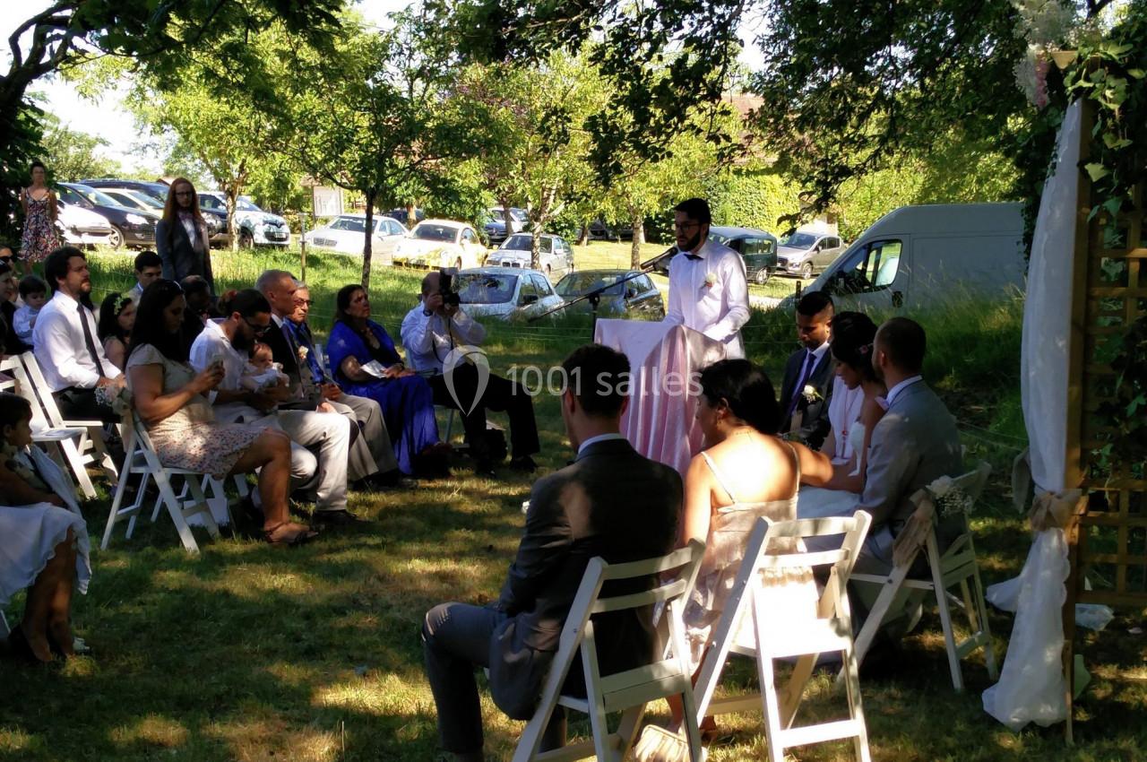 Cérémonie de mariage en plein air avec des invités assis sur des chaises blanches, entourés d'arbres et de voitures en…