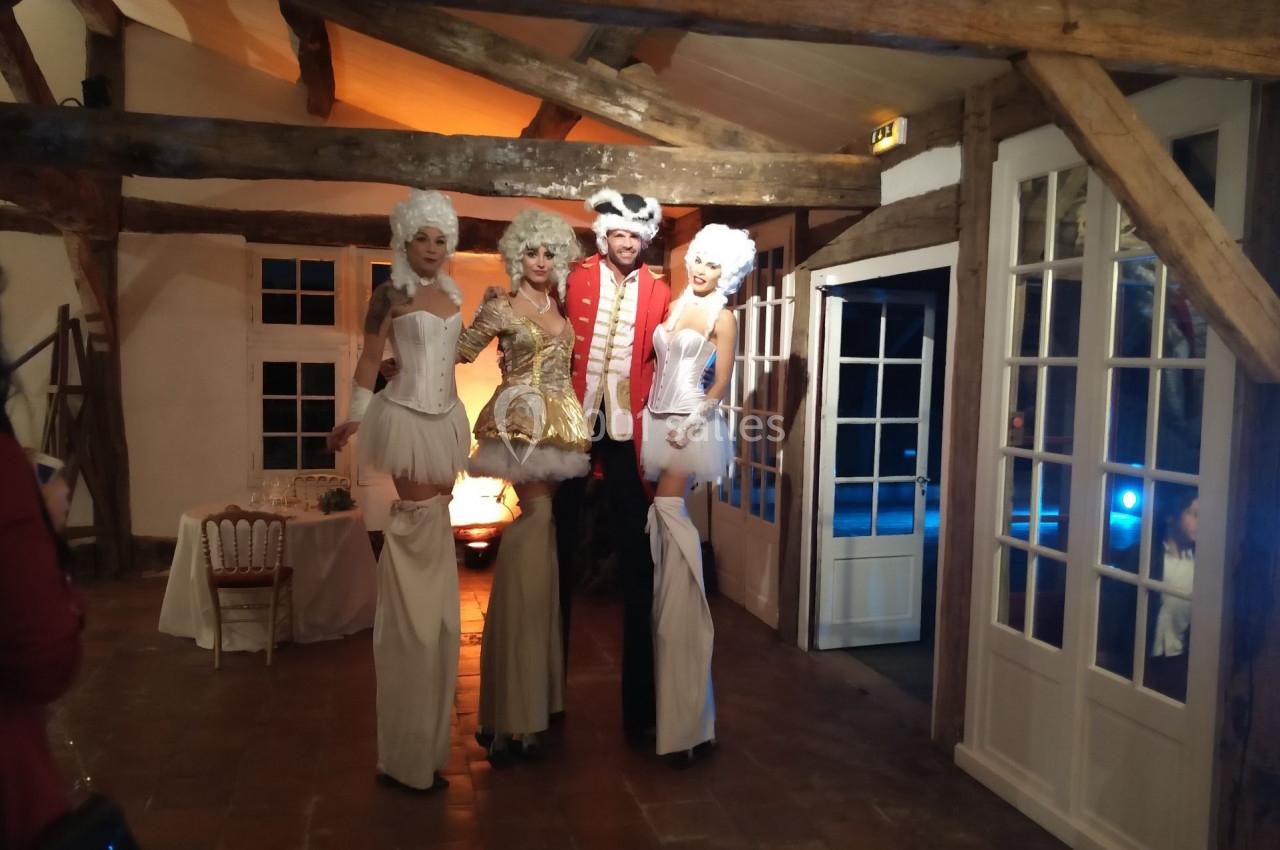 Des artistes en costumes d'époque posent dans une salle rustique avec poutres apparentes et éclairage chaleureux.