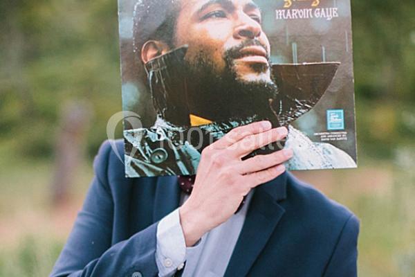 Un homme en costume tient une pochette de disque vinyle devant son visage, alignant le portrait avec sa tête.