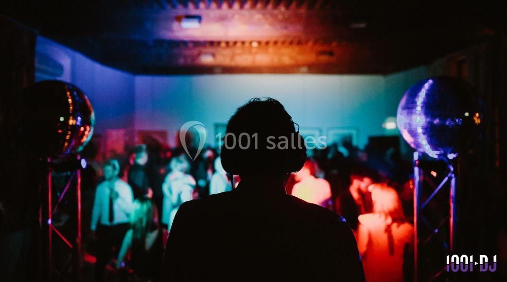 Une silhouette de DJ au premier plan avec une foule dansante éclairée par des lumières colorées en arrière-plan.