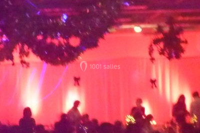 Façade en pierre éclairée par des lumières violettes et bleues, avec des tables en métal noir au premier plan.