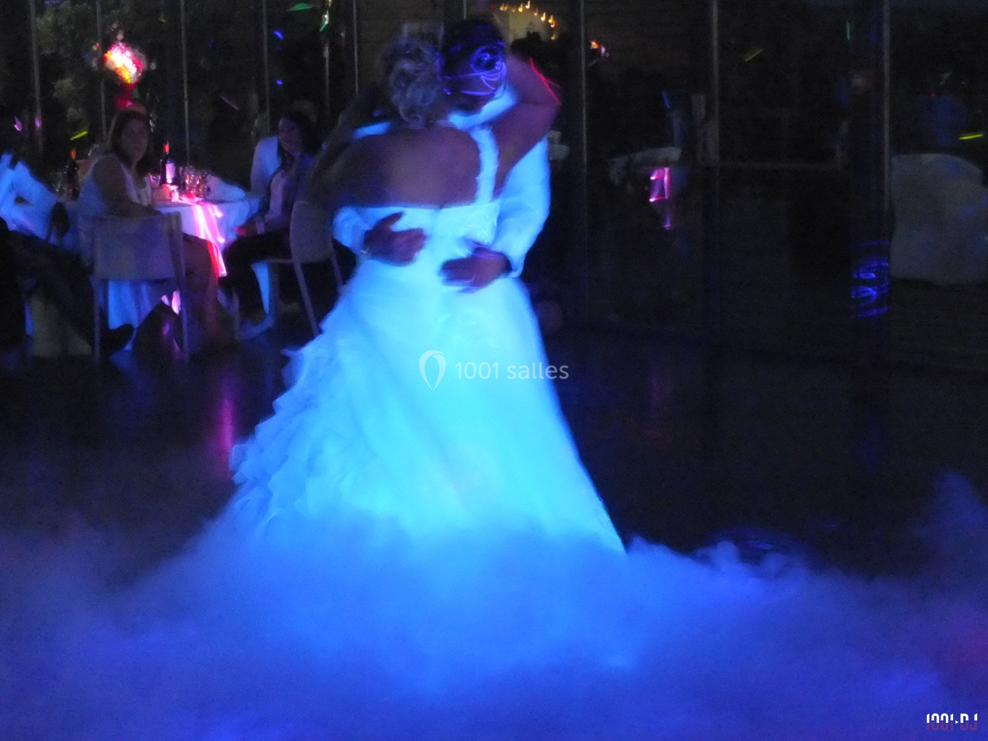 Un couple danse dans une ambiance tamisée avec éclairages colorés et fumée au sol.