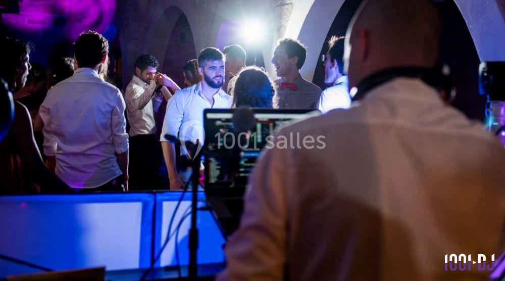 Un DJ anime une soirée dansante avec des invités discutant et dansant sous des lumières colorées.