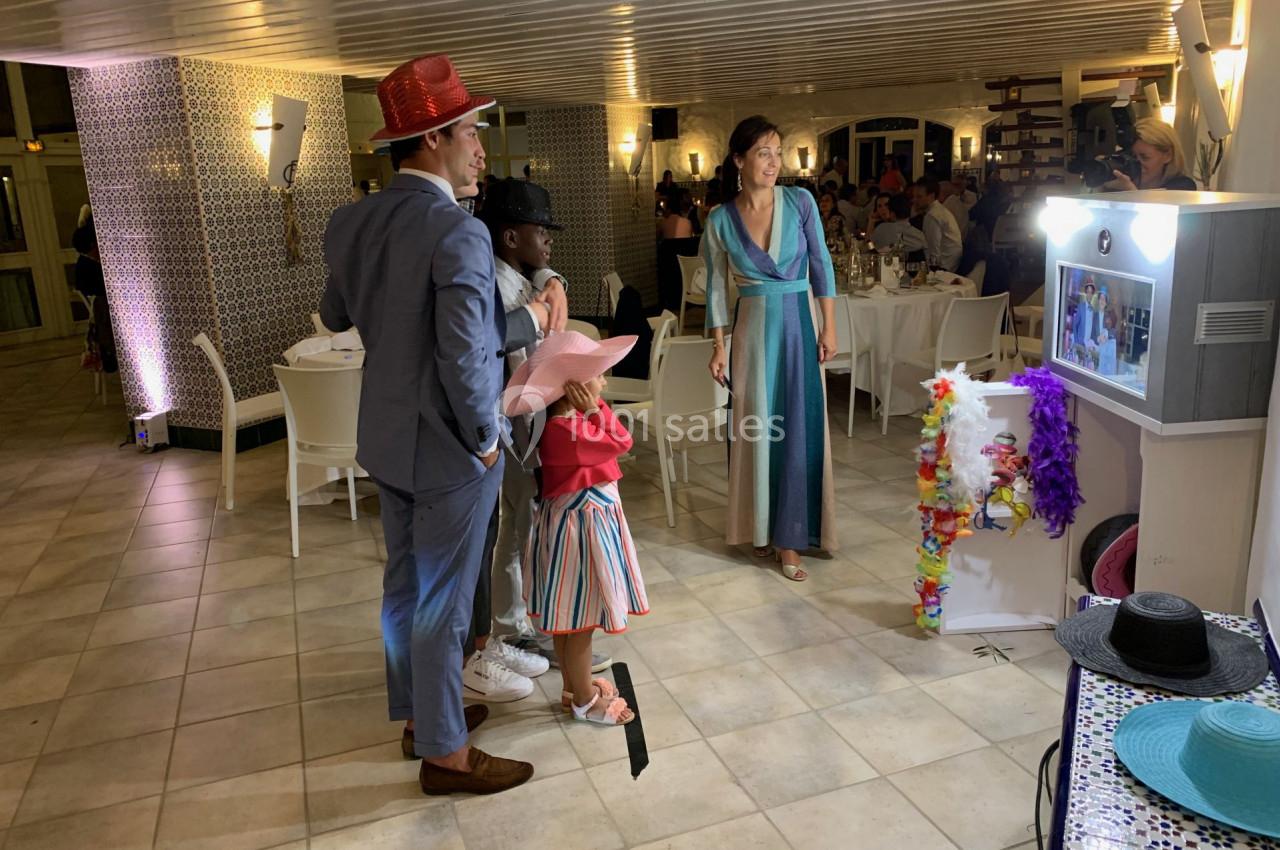 Des personnes déguisées avec des chapeaux colorés utilisent une borne photo dans une salle de réception éclairée.