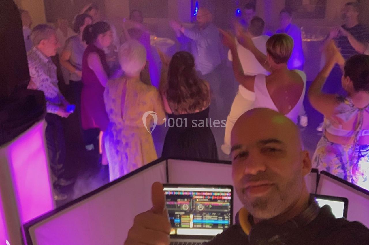 Un DJ anime une soirée dansante avec des invités qui dansent sous des lumières colorées.