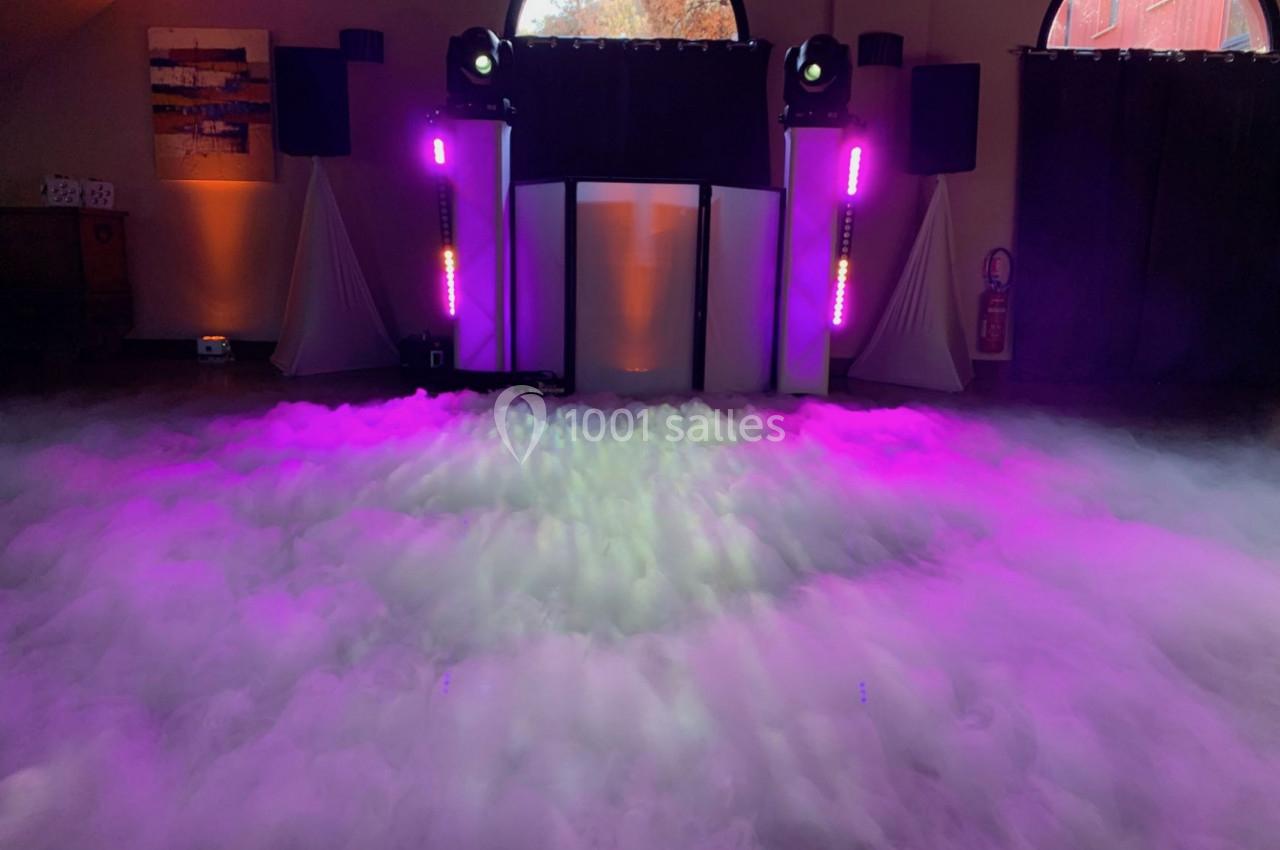 Salle décorée pour un événement avec éclairage violet, machines à fumée et équipements audio devant une baie vitrée.