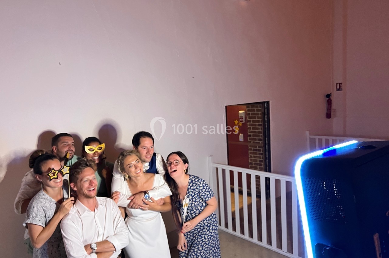 Un groupe de personnes souriantes pose avec des accessoires ludiques devant une borne photo dans une salle éclairée.