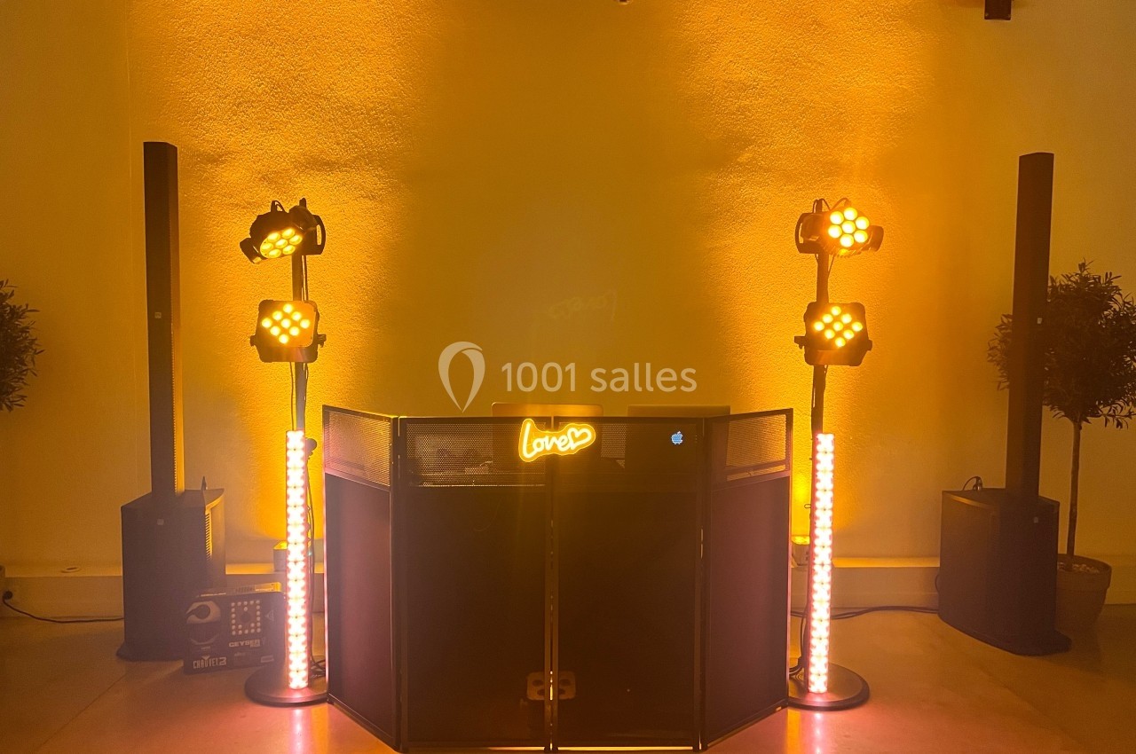 Poste de DJ éclairé par des lumières jaunes et orange, entouré de projecteurs et de colonnes lumineuses.