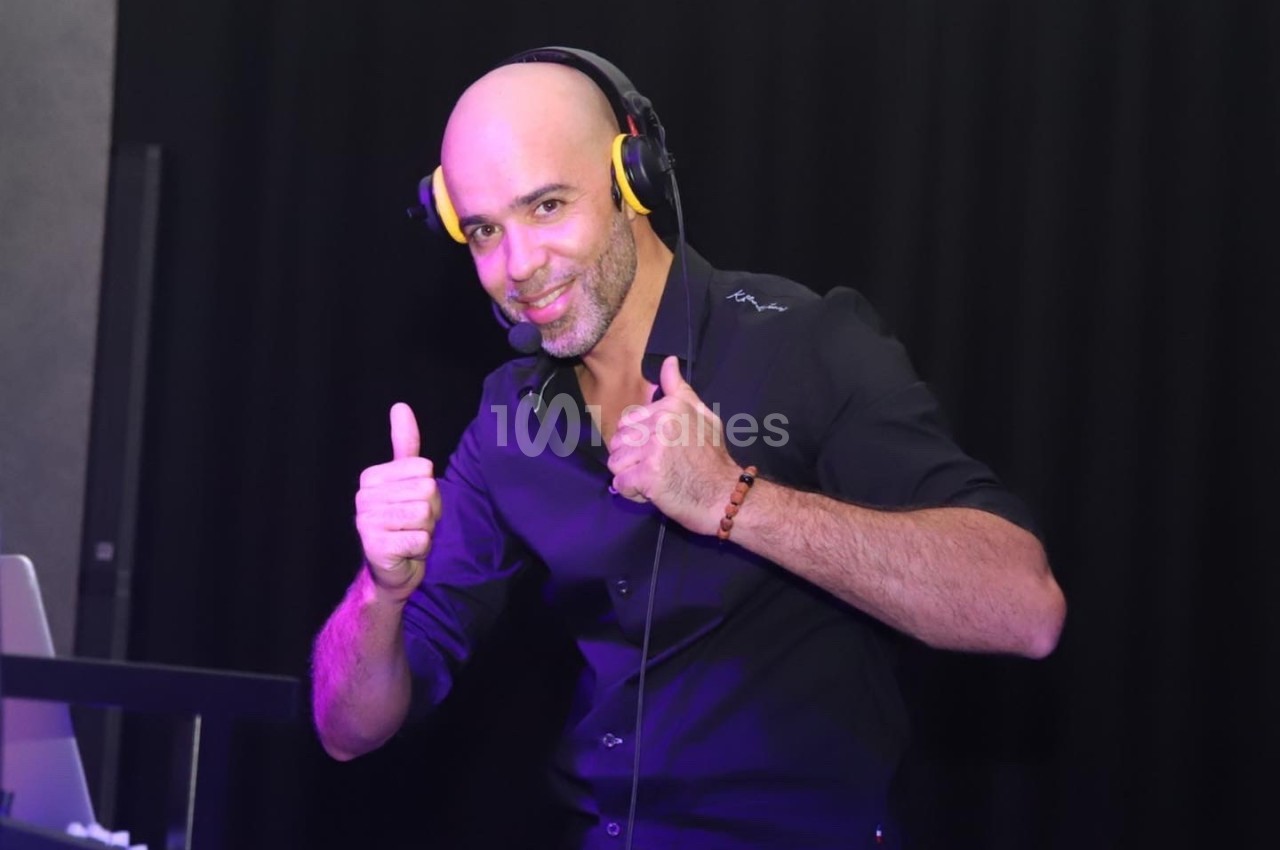 Homme souriant portant un casque audio, levant les pouces, devant un fond sombre.