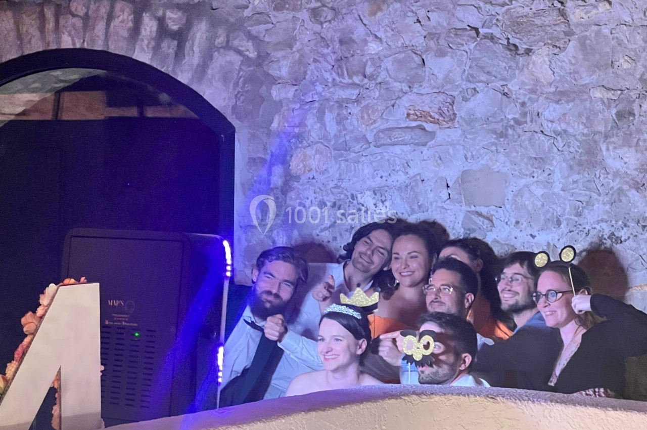 Un groupe de personnes souriantes pose avec des accessoires festifs devant un mur en pierre.