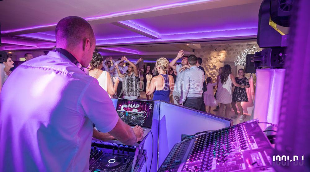 Un DJ anime une soirée dansante dans une salle éclairée par des lumières violettes, avec des invités sur la piste.