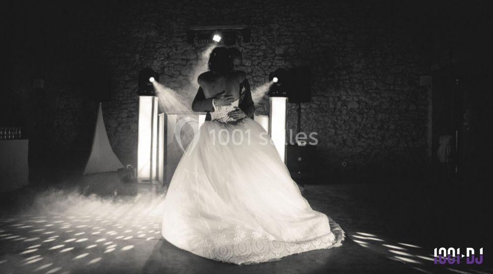 Un couple danse dans une salle sombre éclairée par des projecteurs, la mariée portant une robe blanche.