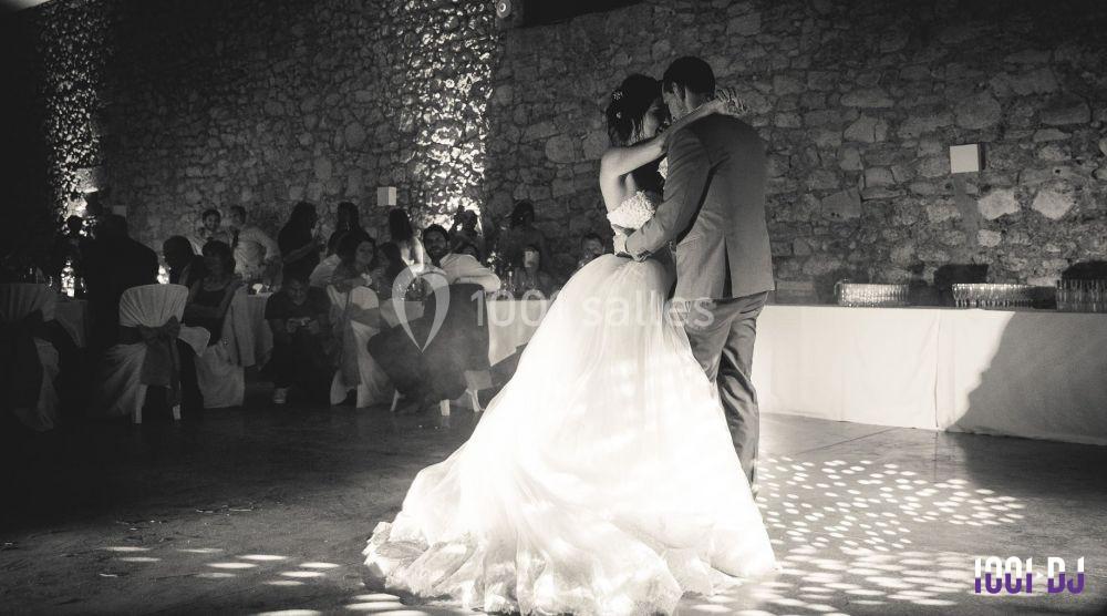 Un couple danse lors d'une réception de mariage dans une salle en pierre, éclairée par une lumière tamisée.