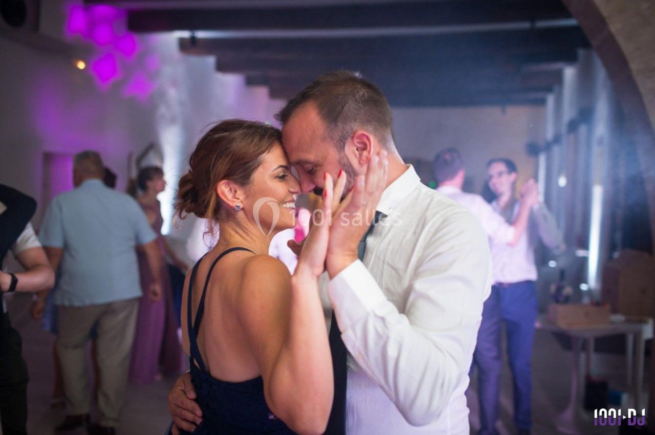 Un couple danse en se tenant par les mains dans une salle éclairée avec des invités en arrière-plan.