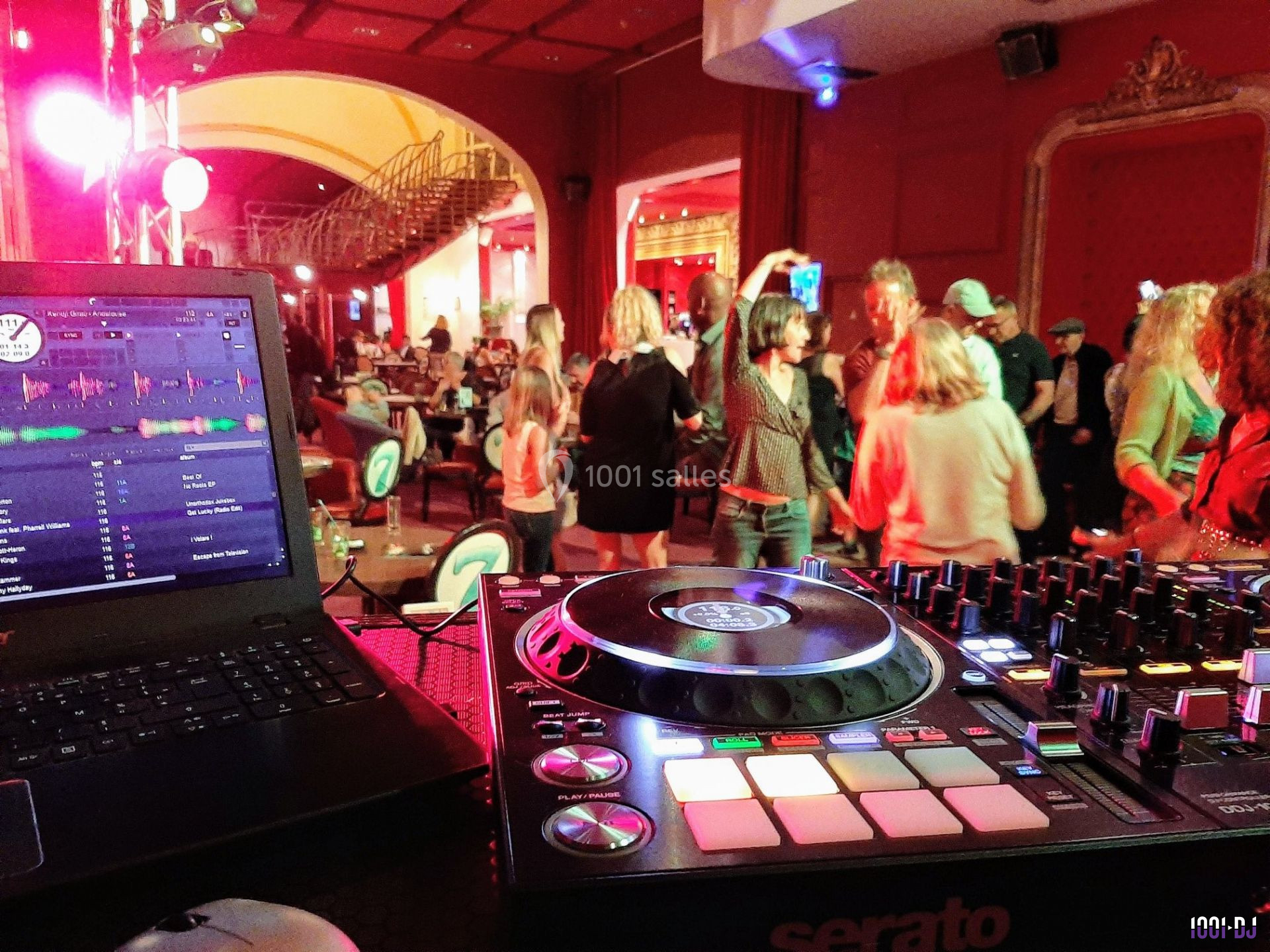 Vue d'une piste de danse animée dans une salle, avec une table de mixage et un ordinateur au premier plan.