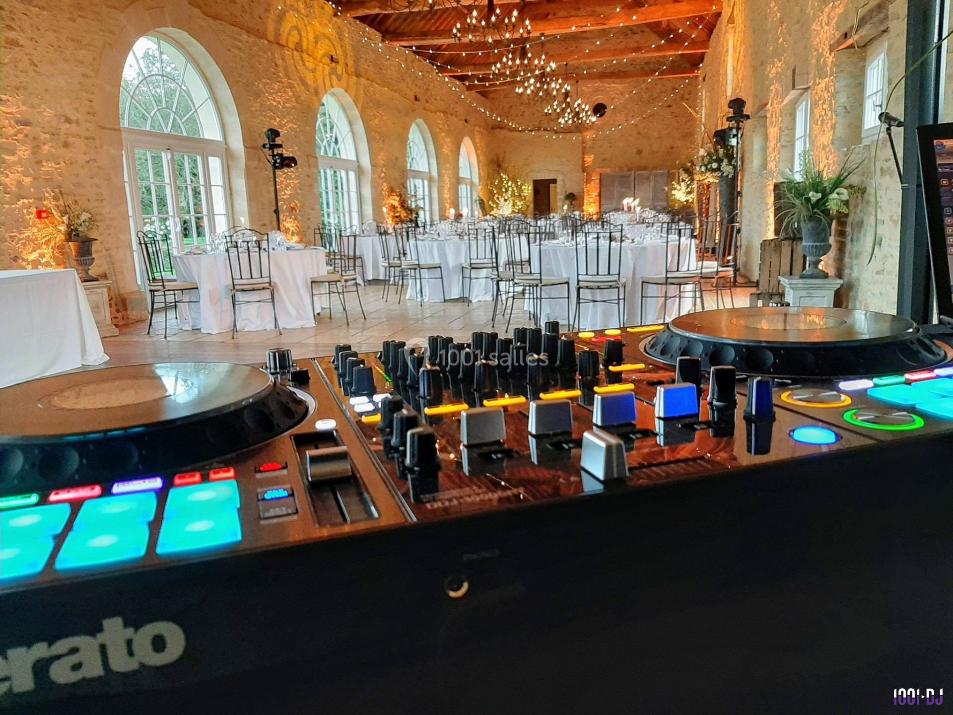 Vue d'une salle de réception élégante avec tables dressées, éclairages suspendus, et une table de mixage au premier plan.