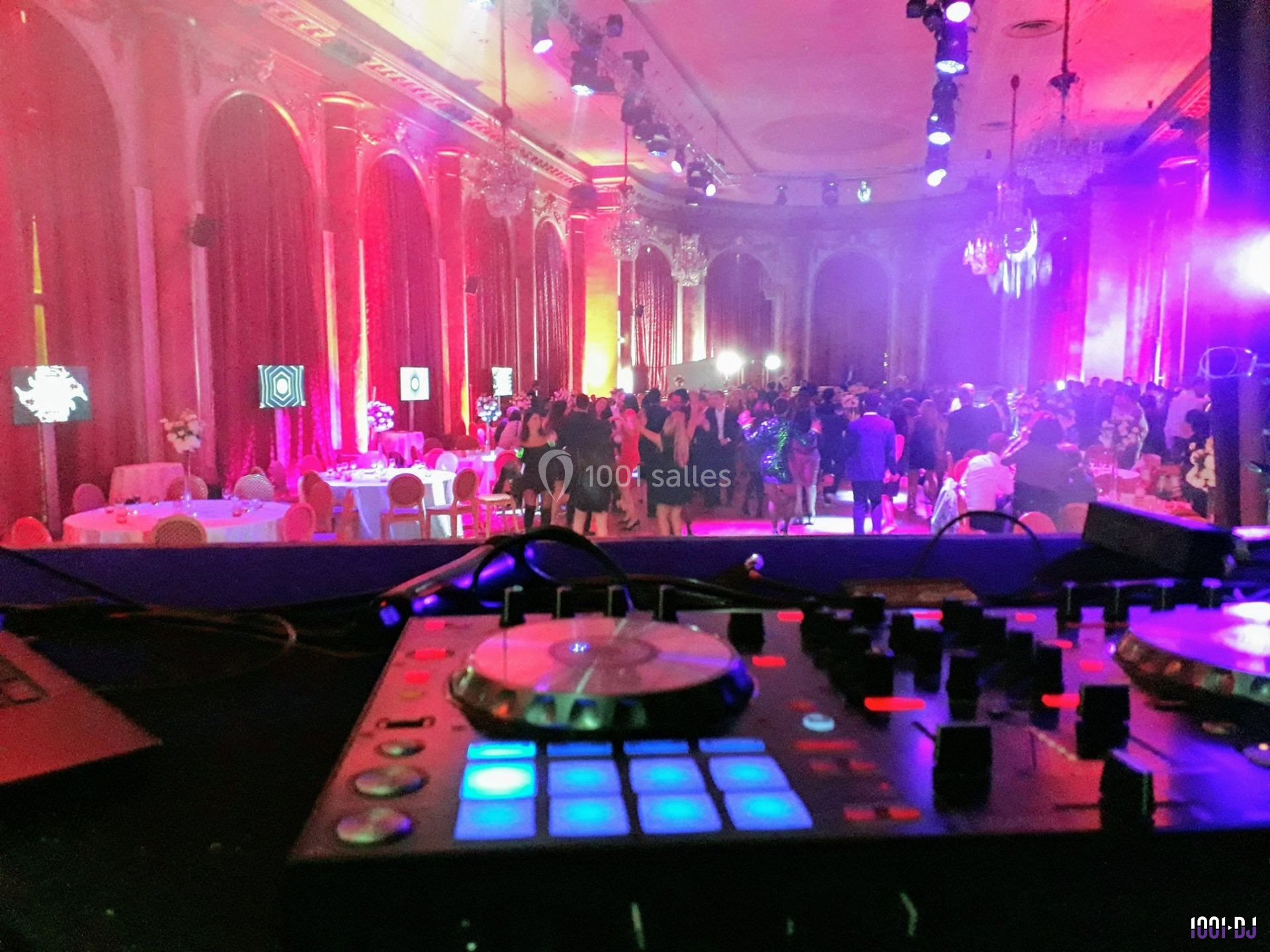 Vue d'une salle de réception illuminée avec des invités, prise depuis une table de mixage en premier plan.