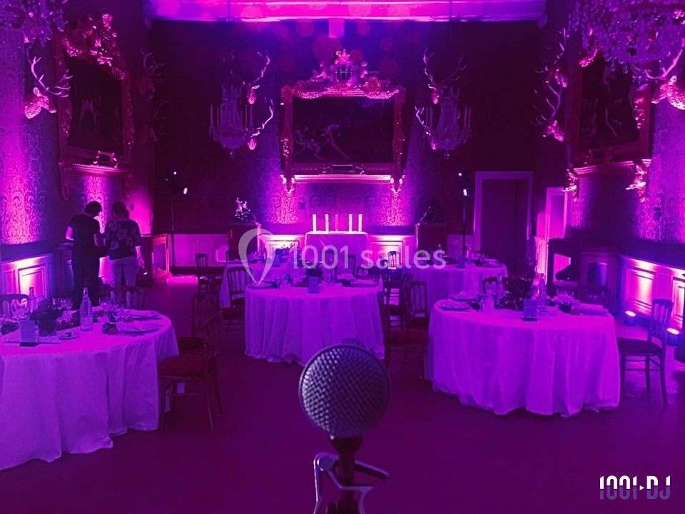 Salle de réception éclairée en violet avec tables rondes dressées et un micro au premier plan.