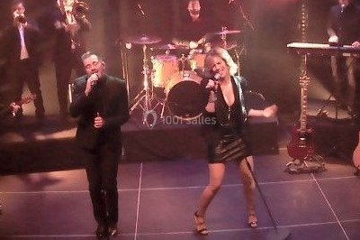 Scène de concert avec batterie, guitares, claviers et micros sous un éclairage coloré.