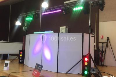 Salle décorée avec des tables dressées, des ballons et une scène équipée d'instruments de musique et de projecteurs.