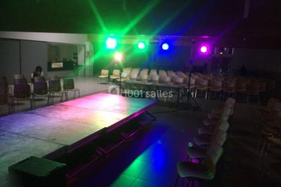 Salle décorée avec des tables dressées, des ballons et une scène équipée d'instruments de musique et de projecteurs.
