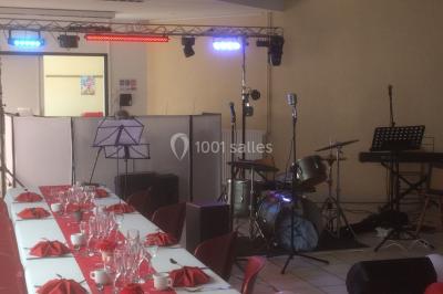 Salle décorée avec des tables dressées, des ballons et une scène équipée d'instruments de musique et de projecteurs.