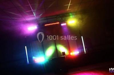 Salle décorée avec des tables dressées, des ballons et une scène équipée d'instruments de musique et de projecteurs.