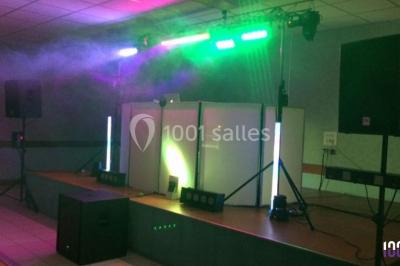 Salle décorée avec des tables dressées, des ballons et une scène équipée d'instruments de musique et de projecteurs.